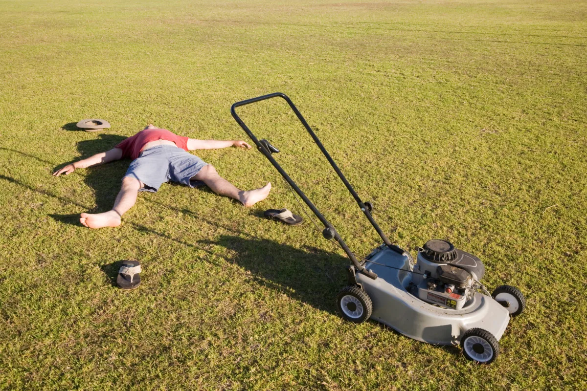 Many laying in grass next to lawn mower completely exhausted.